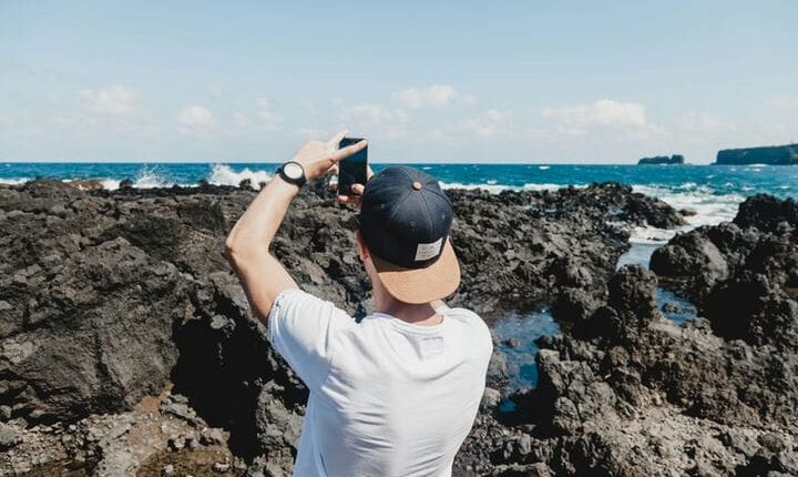 man holding black smartphone while taking a photo of open sea