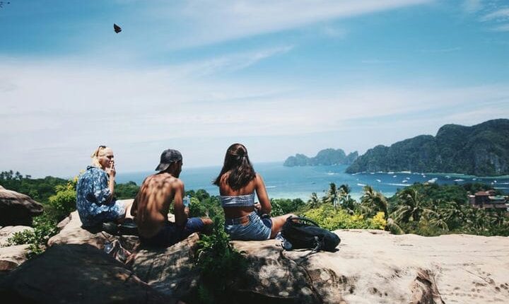 topless man sitting between two persons near body of water