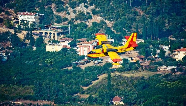 yellow and red plane flying over green grass field during daytime
