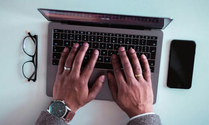man using laptop between eyeglasses and iPhone